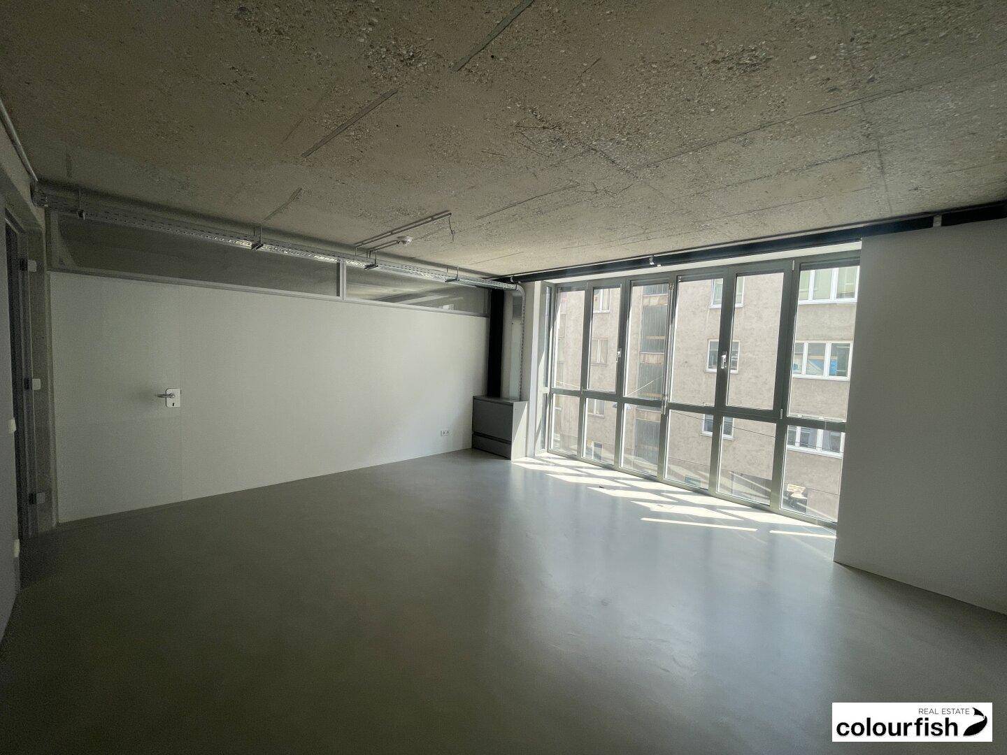 Heller Büroraum mit großer Fensterfront, die viel Tageslicht hereinlässt.