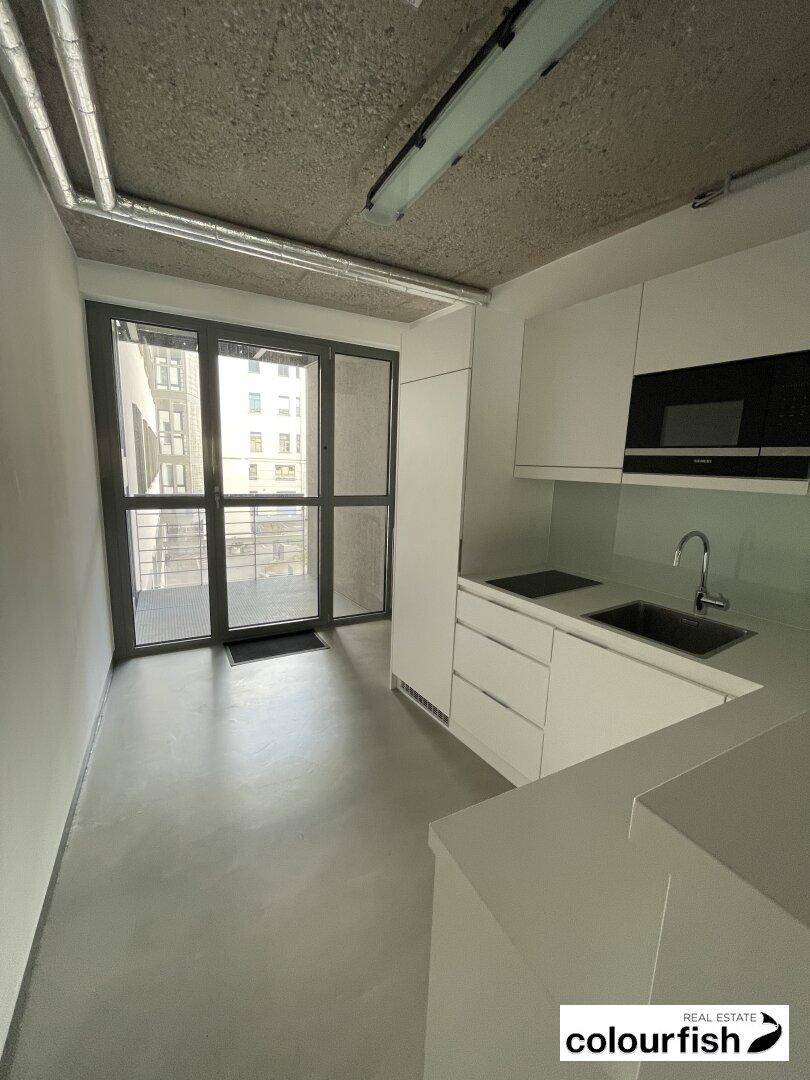 Moderne Küchenzeile mit weißen Schränken, integrierten Geräten und Zugang zu einem Balkon.