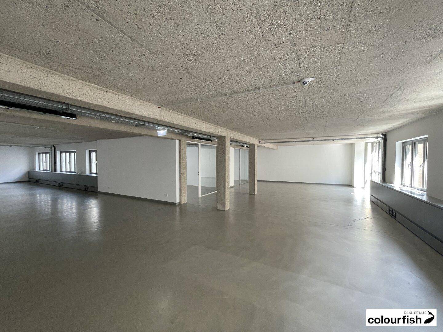 Weitläufiger, heller Bürobereich mit minimalistischem Design und großen Fensterfronten.