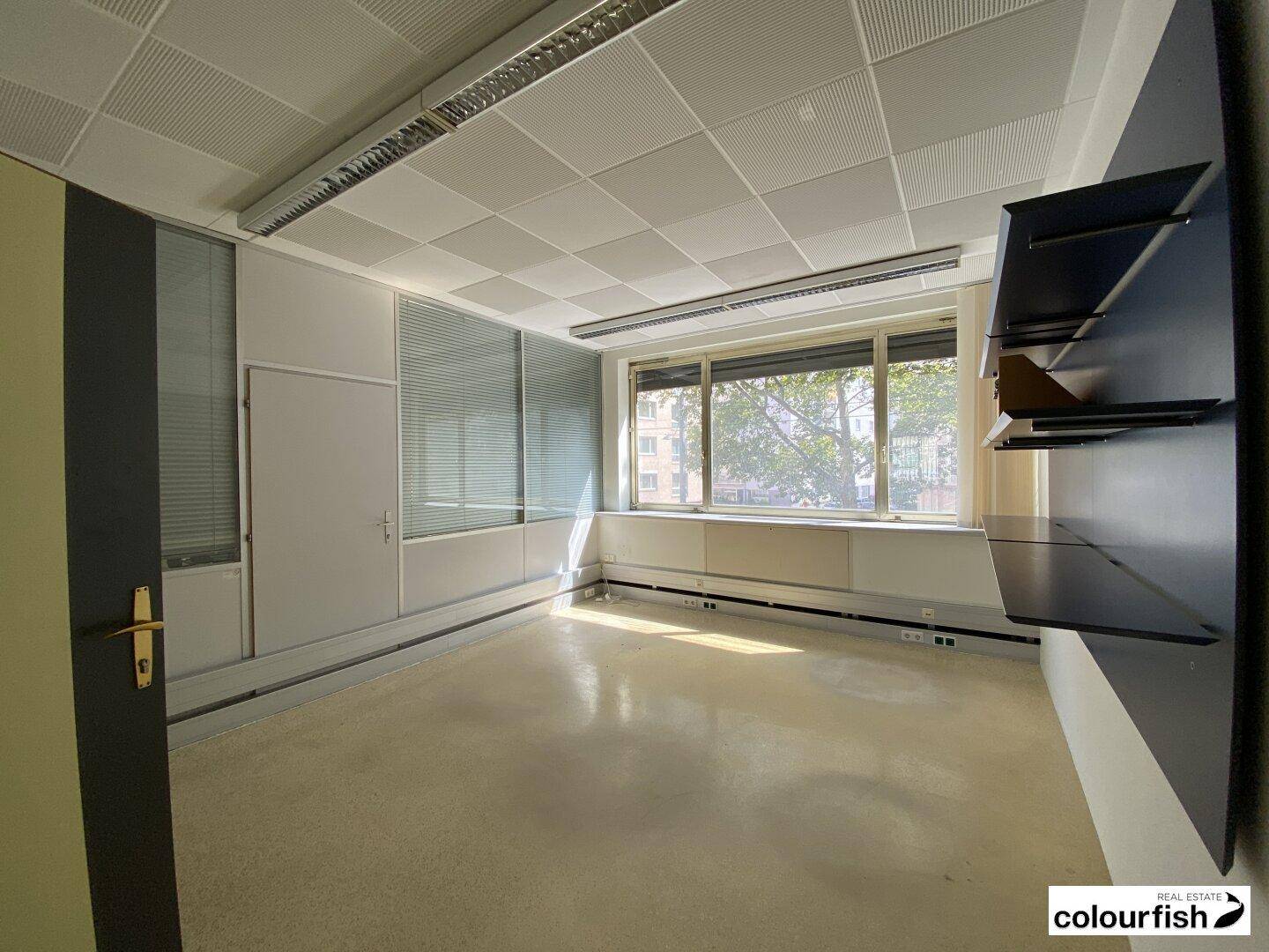 Helles Büro mit Fensterfront, Jalousien und integrierten Wandregalen.