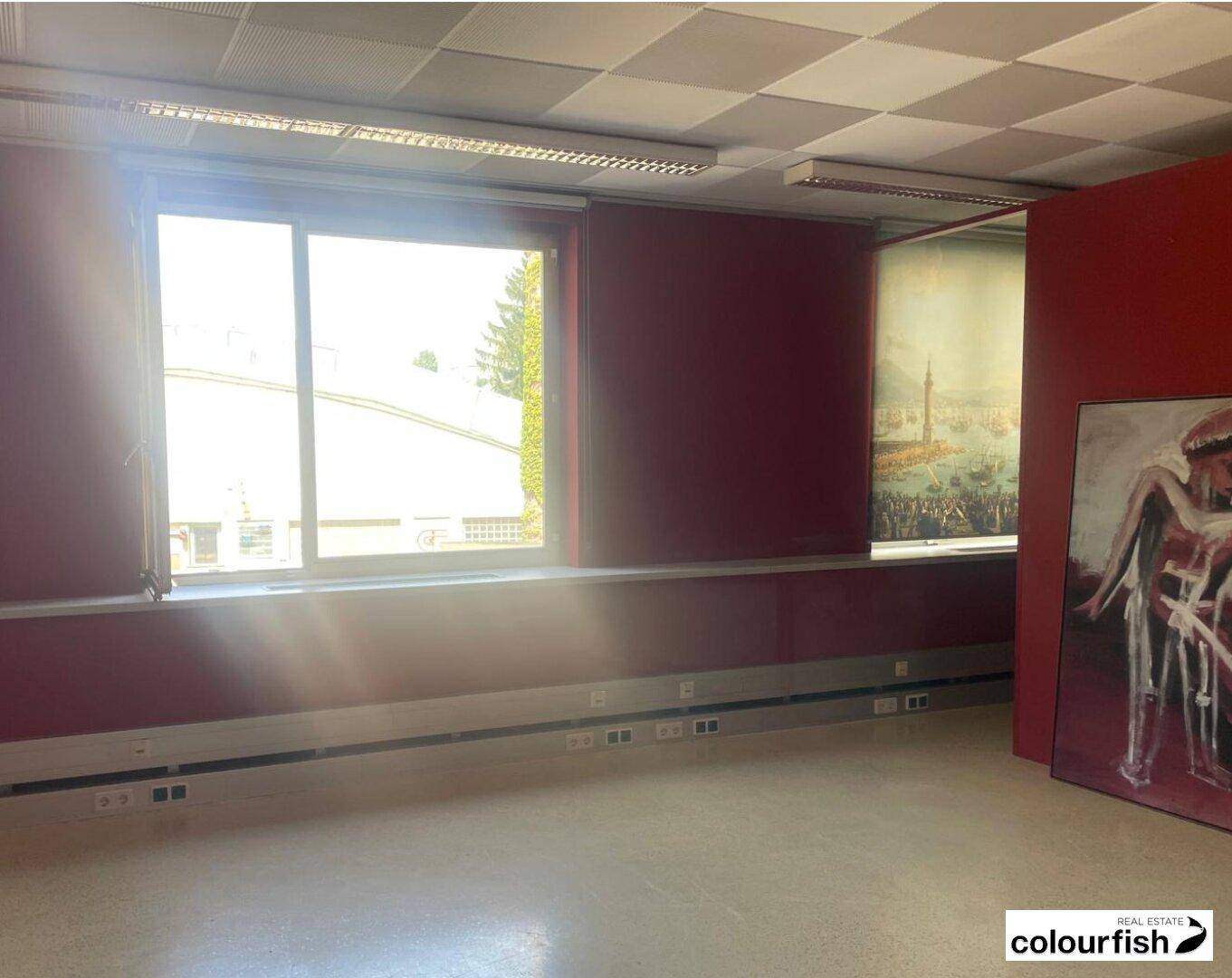 Leeres Büro mit roten Wänden, großen Fenstern und viel Tageslicht.
