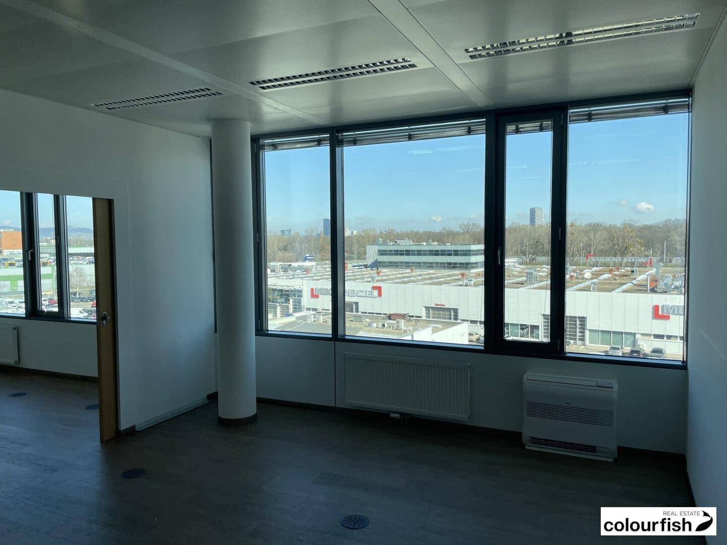 Büroecke mit großen Fenstern, die einen Blick auf ein Gewerbegebiet bieten, ausgestattet mit Heizung und Klimaanlage.
