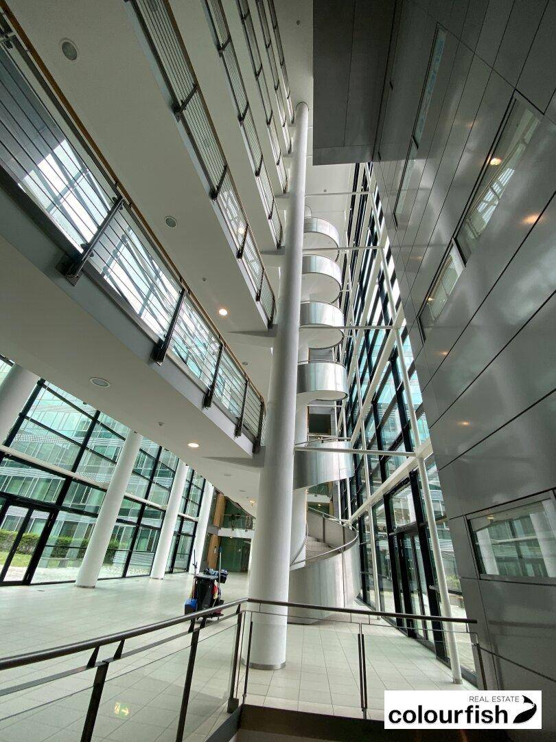 Geräumige und helle Lobby mit moderner Wendeltreppe und großen Glasfronten, die viel Tageslicht hereinlassen.