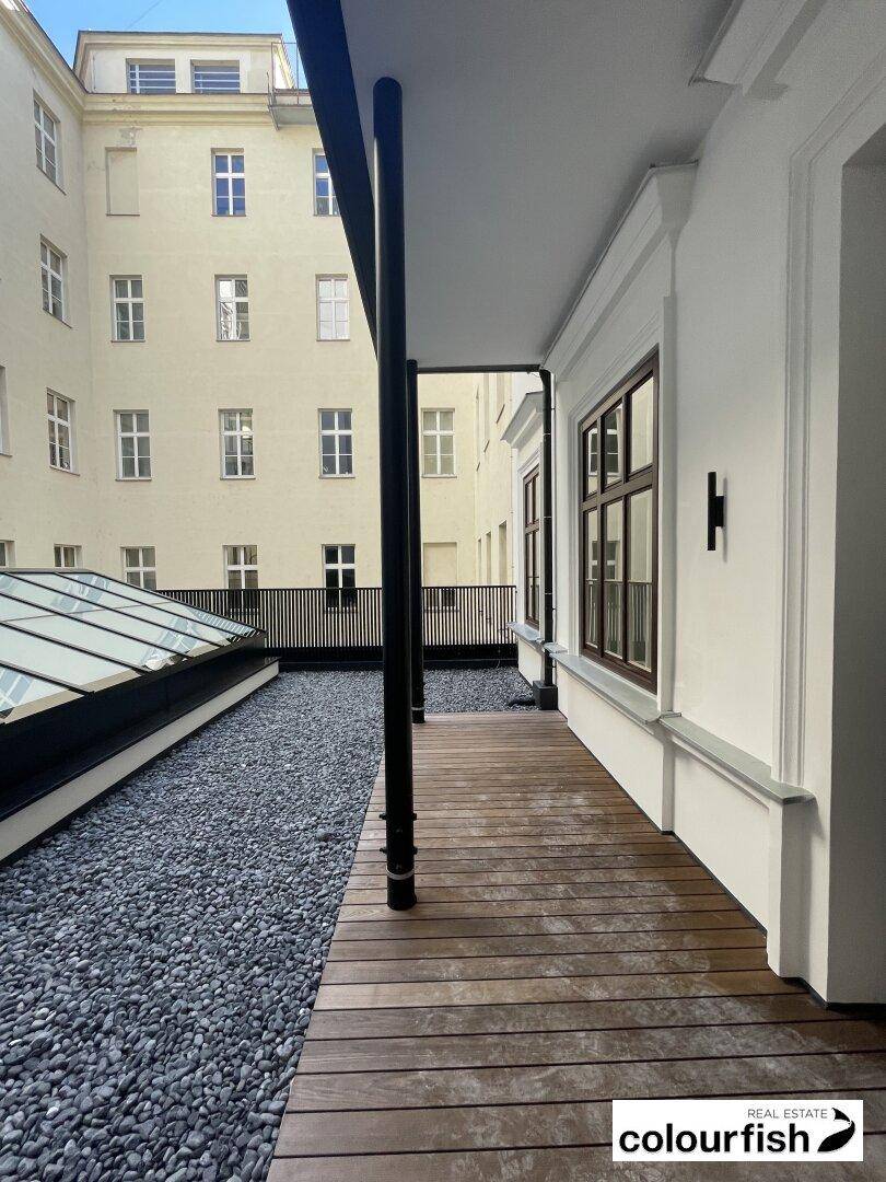 Geräumige Außenterrasse mit Holzboden und Kiesflächen, umgeben von Gebäudefassaden.