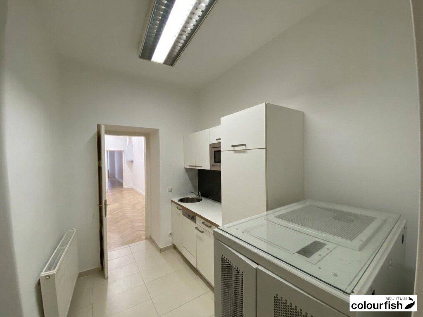 Funktionale Küchenzeile mit weißen Schränken und Fliesenboden, daneben ein technischer Schrank.