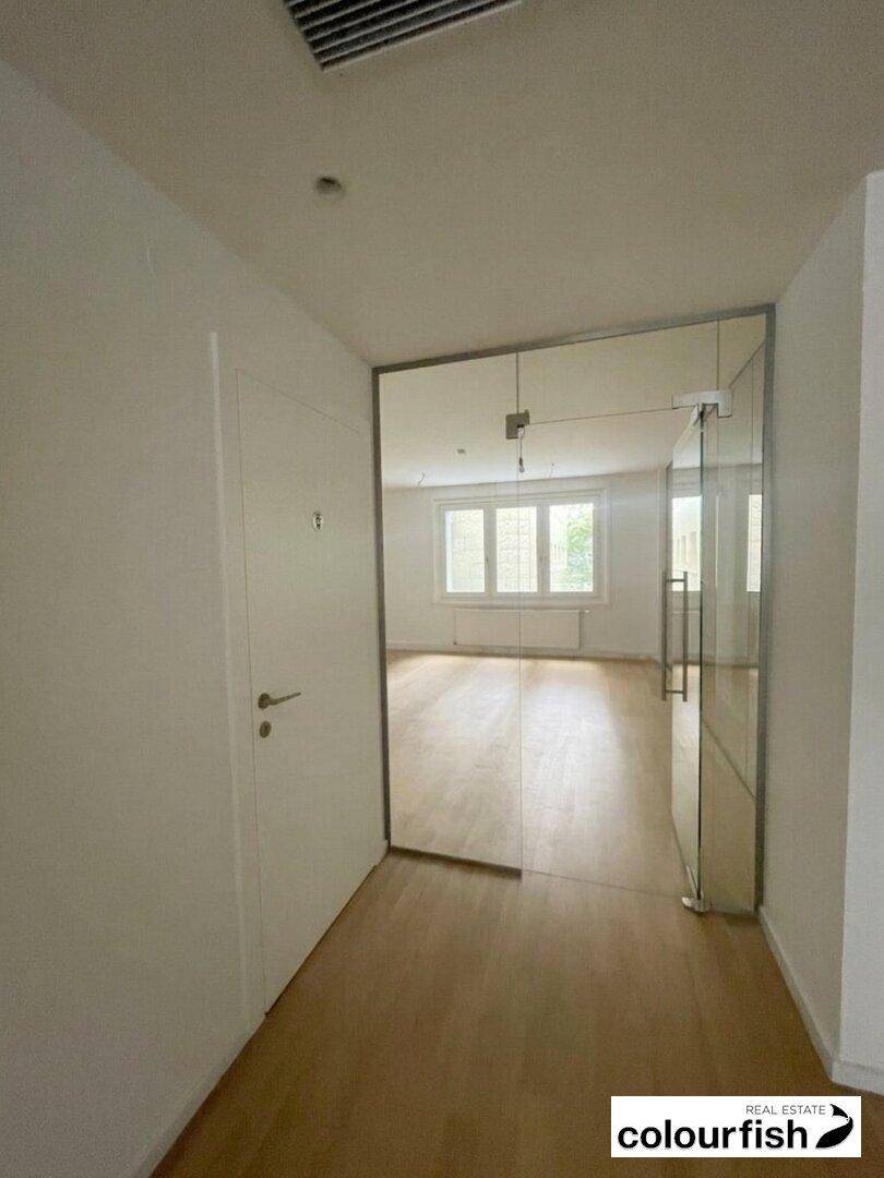 Heller Flur mit Holzboden und einer modernen Glastür, die zu einem weiteren Raum führt.