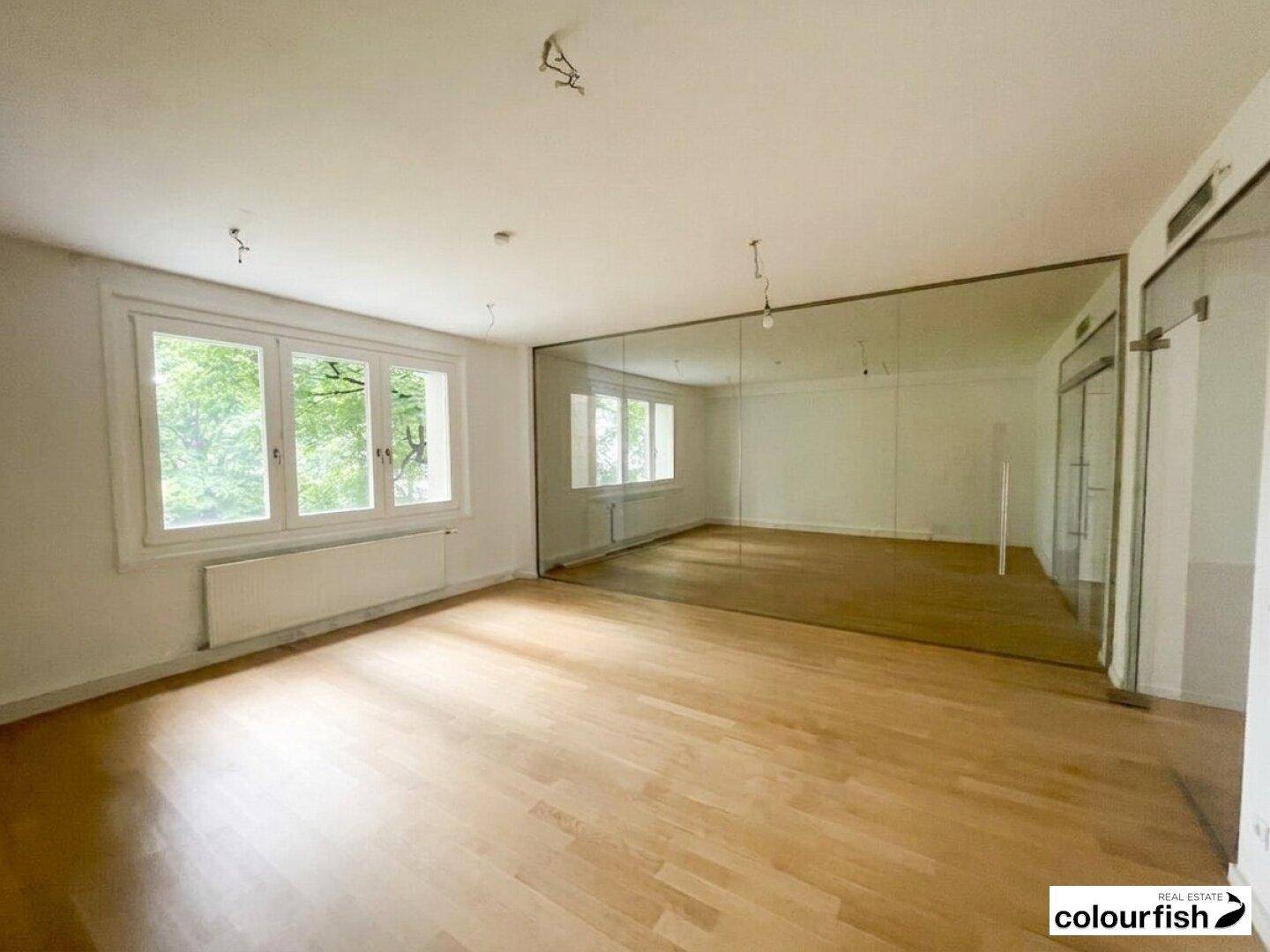 Heller Büroraum mit großen Fenstern, Holzboden und einer langen Glaswand, die den Raum optisch erweitert.