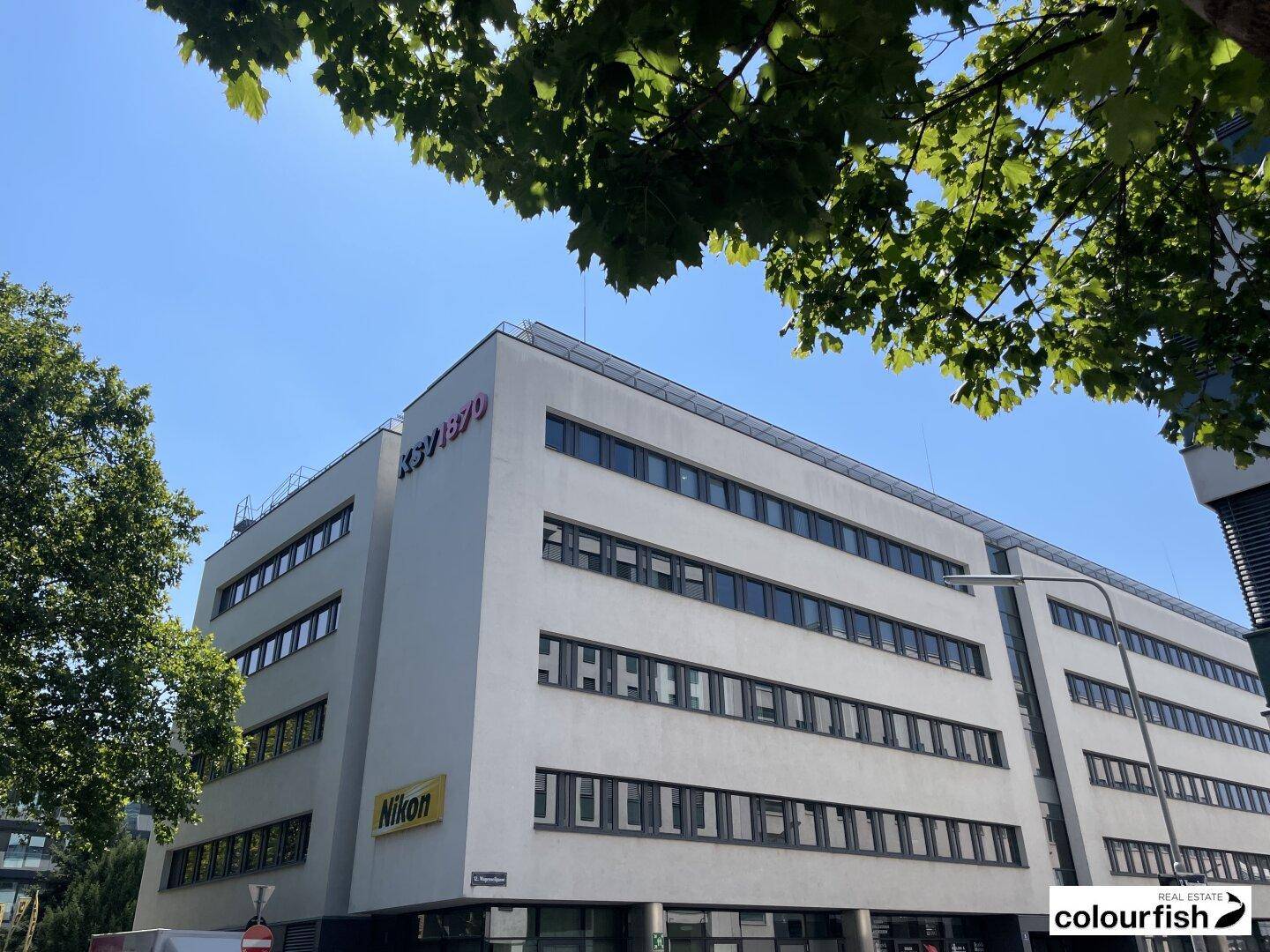 Modernes Bürogebäude mit vielen Fenstern und klarem blauen Himmel im Hintergrund.