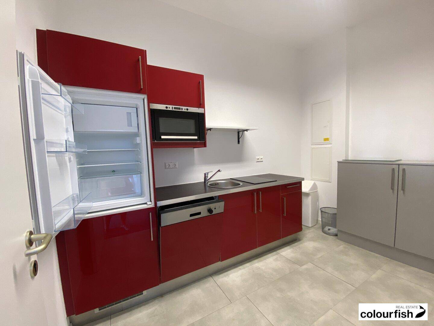 Kleine Küchenzeile mit roten Hochglanzschränken, Kühlschrank, Mikrowelle und Spülmaschine.