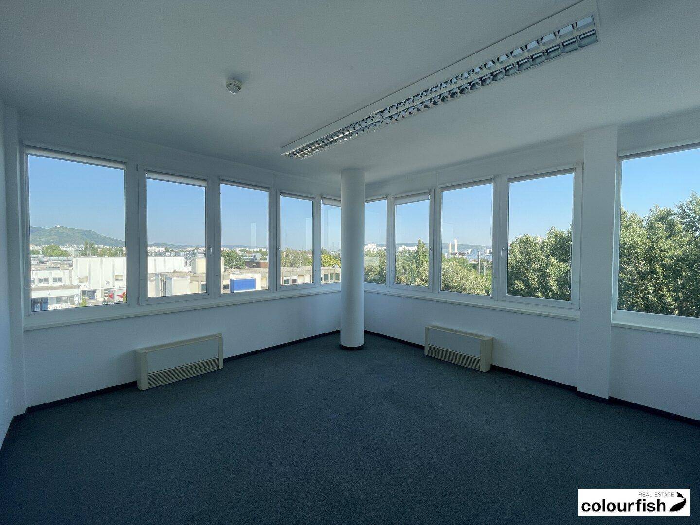 Heller Büroraum mit Teppichboden, vielen Fenstern und weitem Stadtblick.