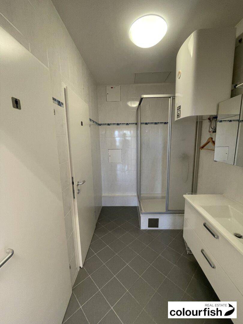 Funktionales Badezimmer mit Duschkabine, Waschbecken und hellen Fliesen.