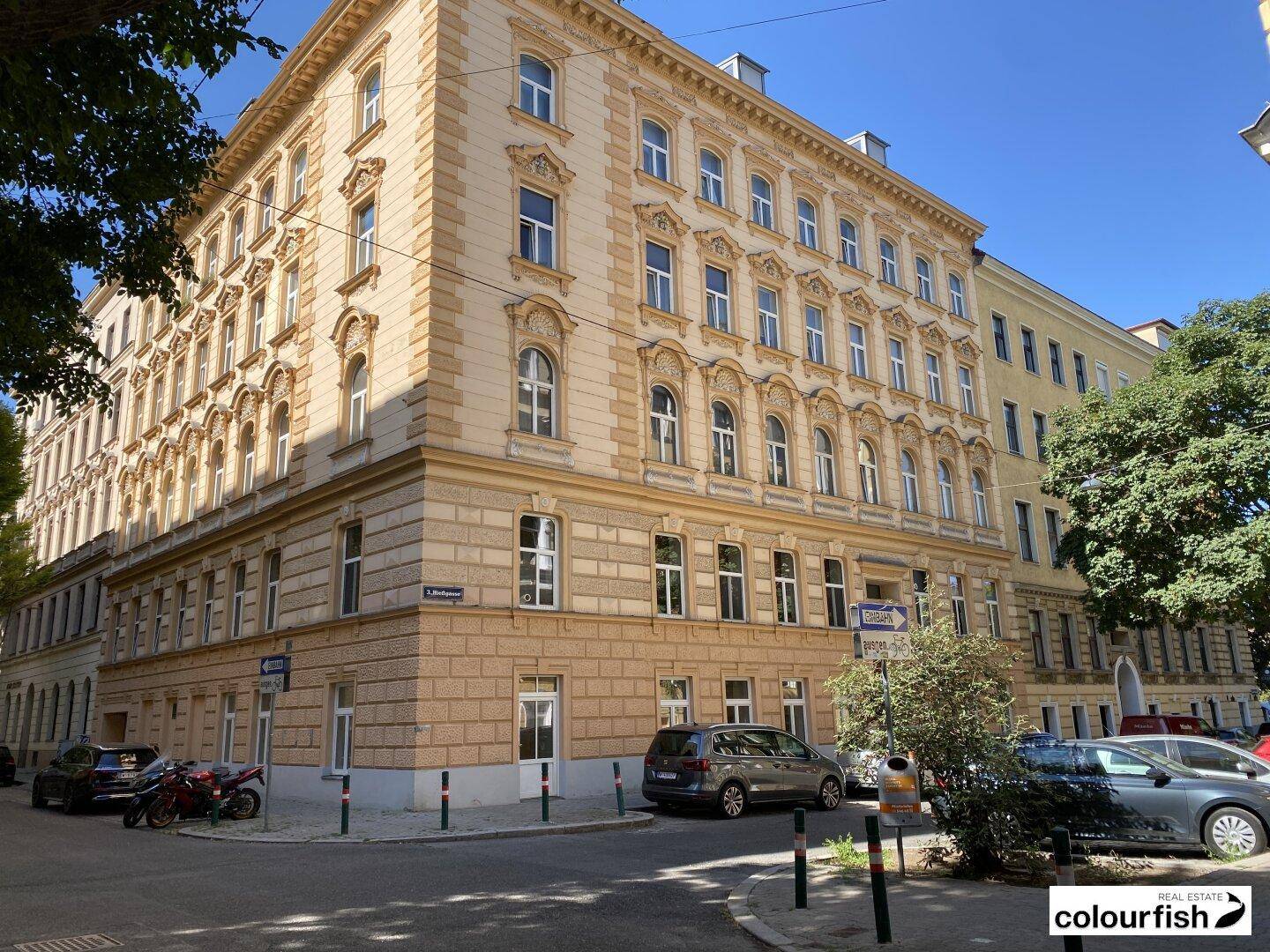 Historisches Eckgebäude mit reich verzierter Fassade und vielen Fenstern an einer belebten Stadtstraße.