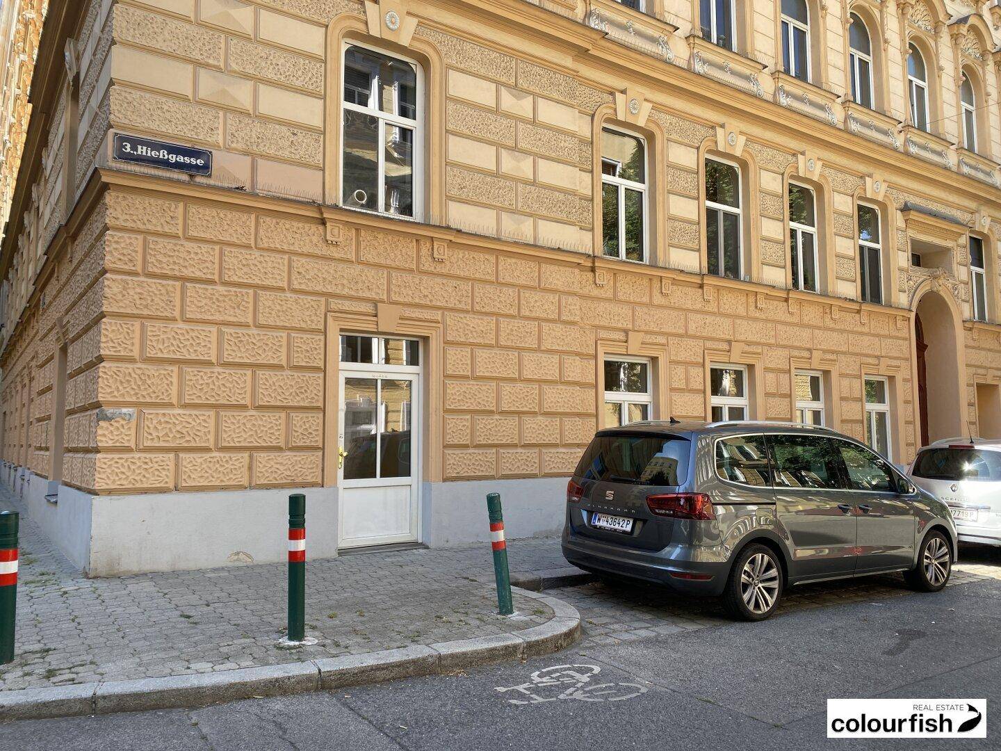 Detailansicht der Erdgeschossfassade eines historischen Gebäudes mit Eingangstür und geparktem Fahrzeug.