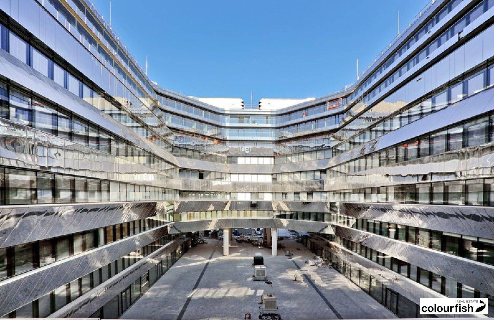 Innenhof eines modernen Bürokomplexes mit spiegelnden Glasfassaden und klarem blauen Himmel.