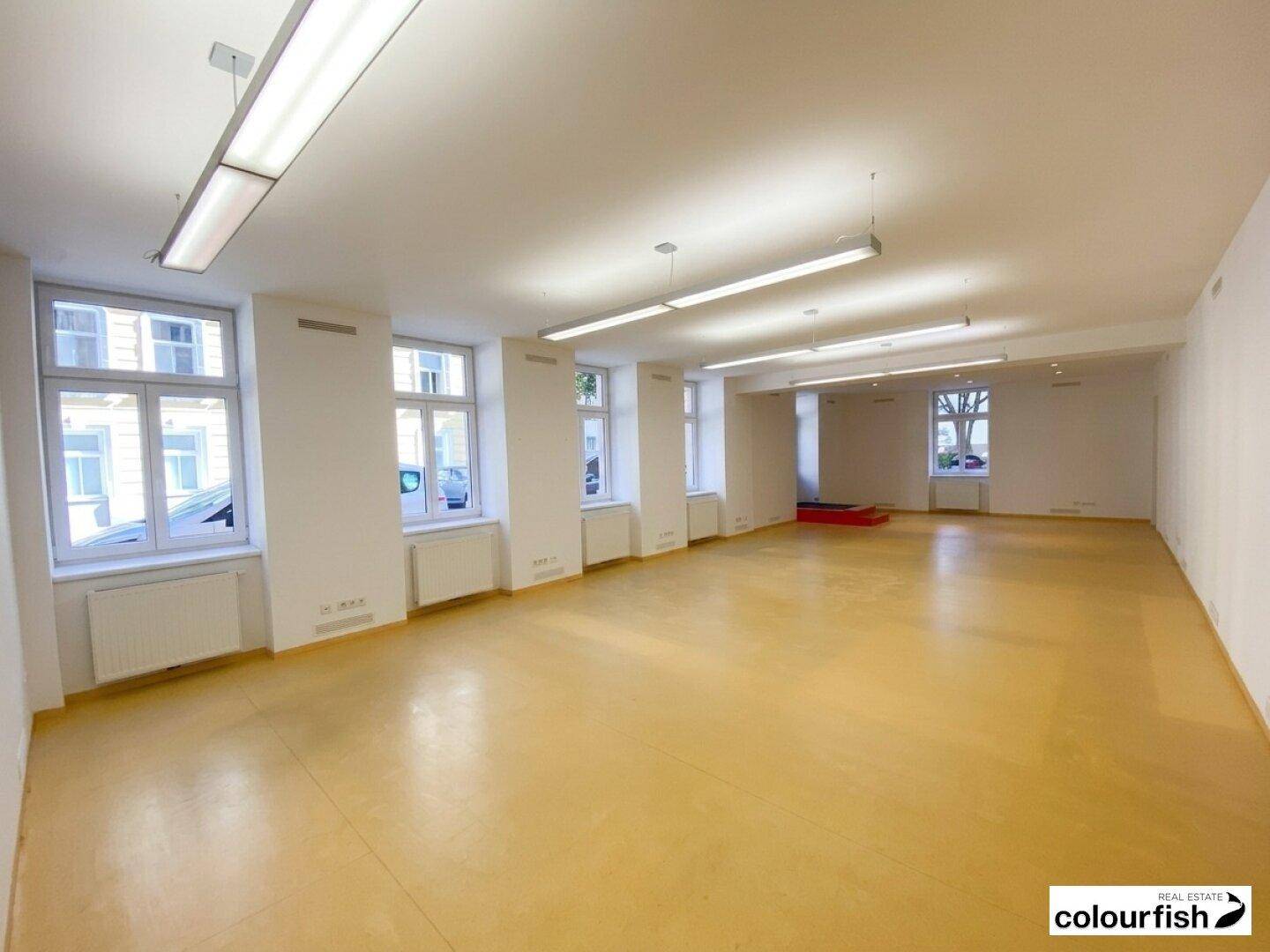 Heller Büroraum mit mehreren Fenstern, Heizkörpern und langen Deckenleuchten, ideal für Arbeitsbereiche.