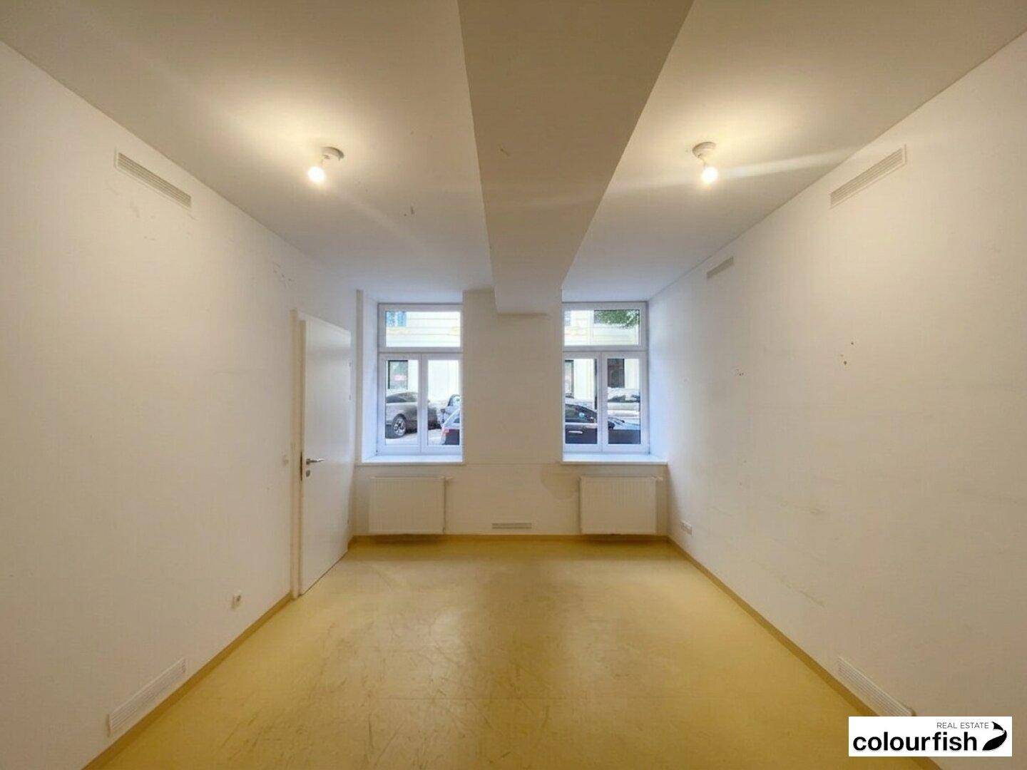 Kleinerer Bürobereich mit zwei großen Fenstern, Heizkörpern und Deckenleuchten, bietet gute Belichtung.