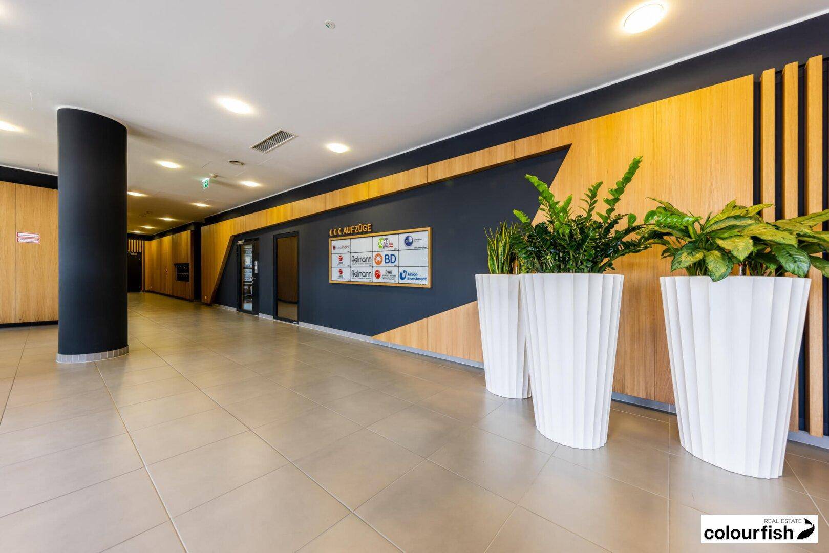 Moderne und einladende Lobby mit Holzvertäfelung, Fliesenboden und Pflanzen als Dekoration.