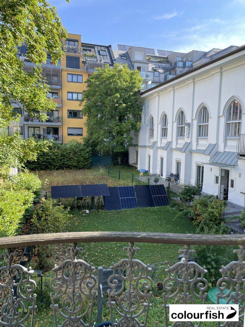 Grüner Gartenbereich mit installierten Solarmodulen und Blick auf die historische Fassade des Gebäudes.