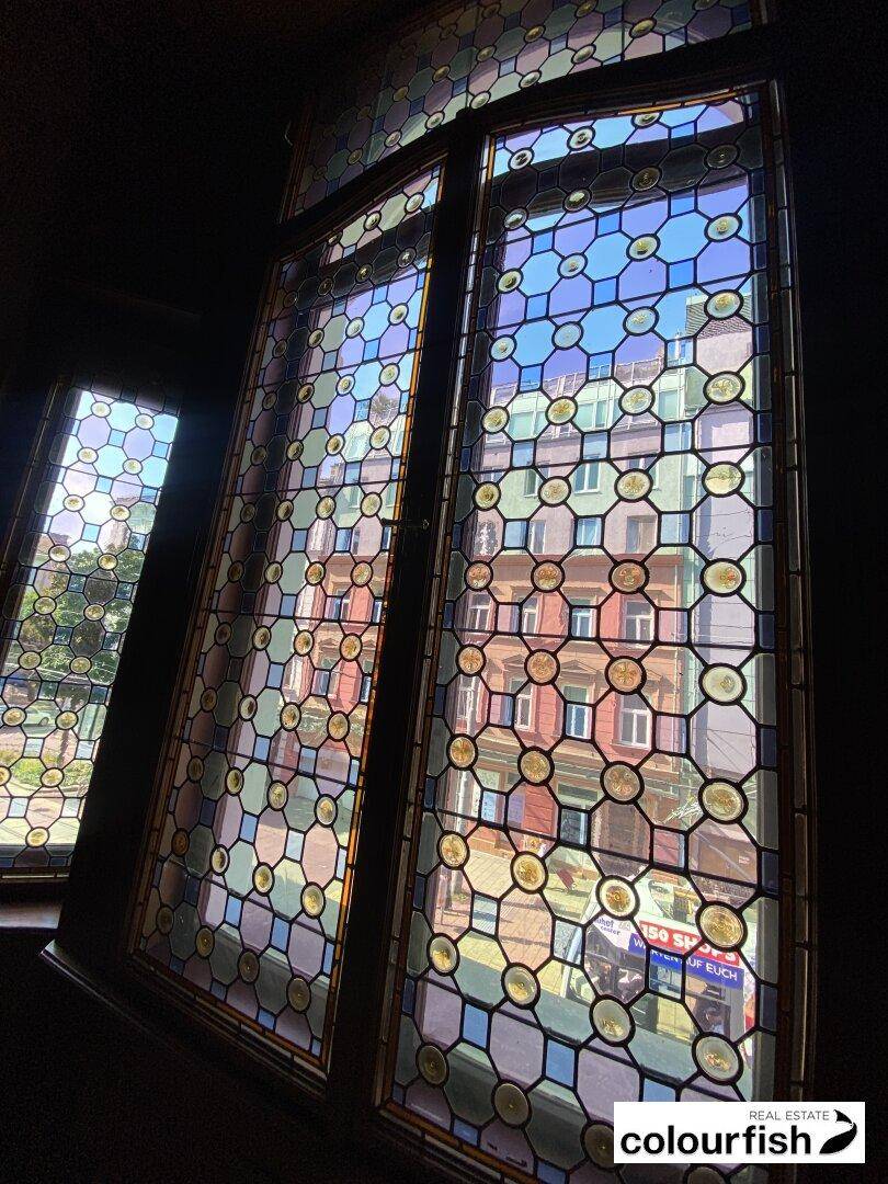 Buntglasfenster mit geometrischen Mustern, die farbenfrohes Licht in den Raum lassen und eine historische Atmosphäre schaffen.