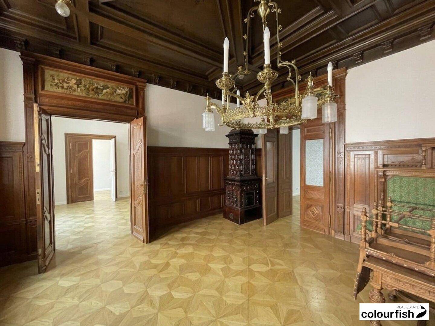 Eleganter Raum mit dunkler Holzvertäfelung, Kronleuchter und einem traditionellen Kachelofen, der Wärme spendet.