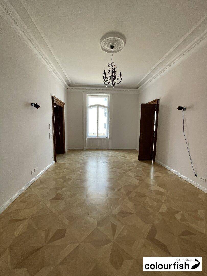 Leerer Raum mit Fischgrätparkett, hohen Decken und einem eleganten Kronleuchter, bereit für individuelle Gestaltung.
