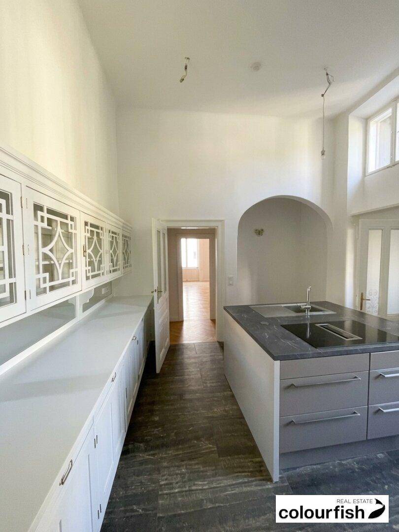 Moderne Küche mit Kücheninsel, dunkler Arbeitsplatte und weißen Oberschränken mit dekorativen Glasfronten.