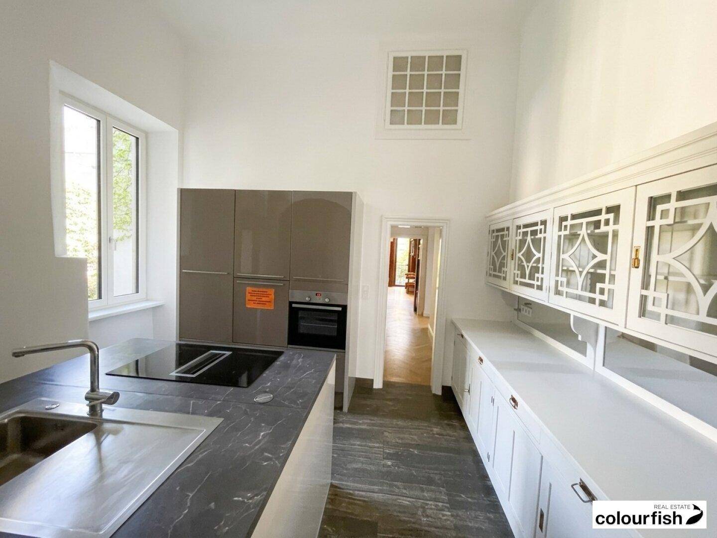 Helle, moderne Küche mit Kücheninsel, integrierten Geräten und einem großen Fenster, das viel Licht hereinlässt.