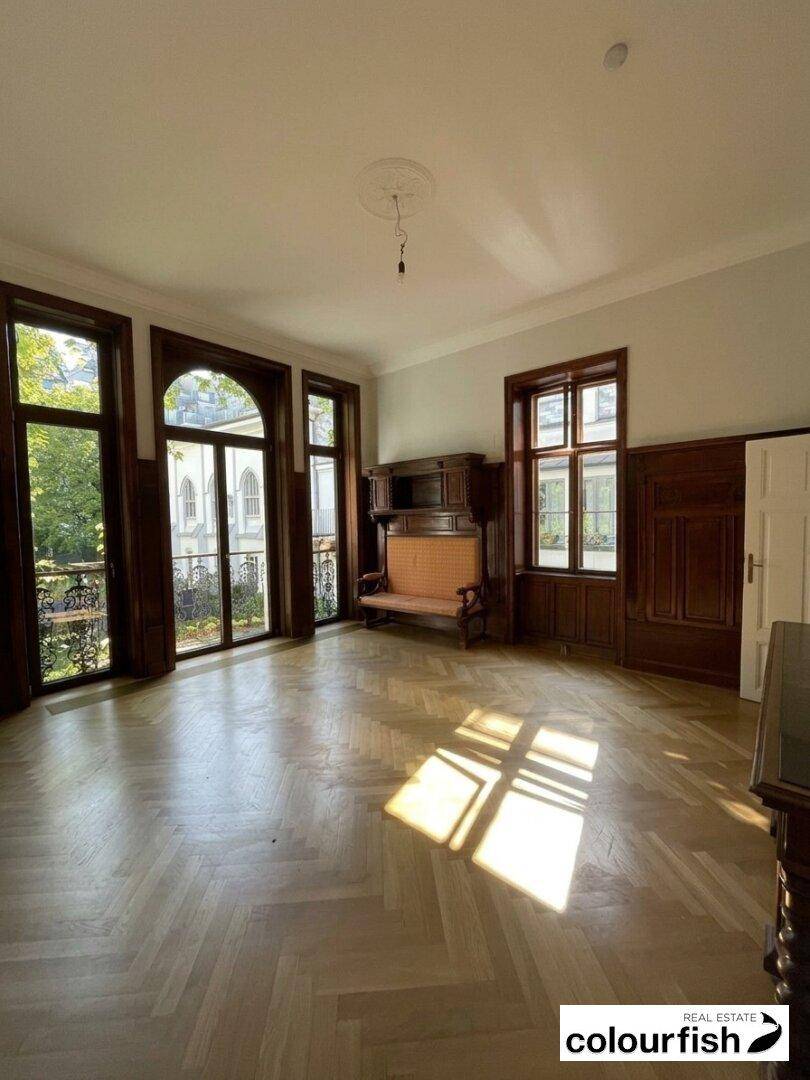 Geräumiger Wohnbereich mit Fischgrätparkett, Holzvertäfelung und viel natürlichem Licht durch hohe Fenster.