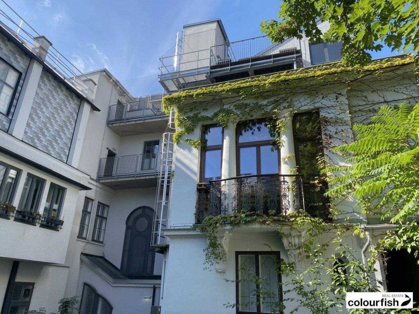 Historisches Gebäude mit mehreren Balkonen, begrünten Fassaden und einem modernen Dachaufbau.