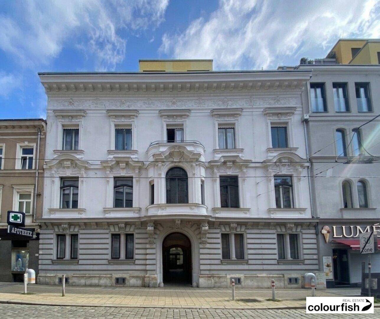 Prächtige historische Fassade eines Altbaus an einer belebten Straße mit Geschäften im Erdgeschoss.
