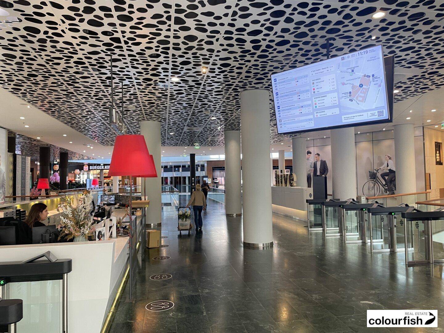 Geräumige, moderne Lobby mit auffälliger Deckenverkleidung, Informationsbildschirm und Zugangskontrolle.