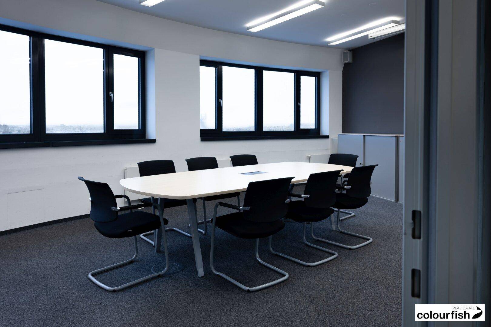 Konferenzraum mit ovalem Tisch, schwarzen Stühlen und großen Fenstern, ideal für Besprechungen.