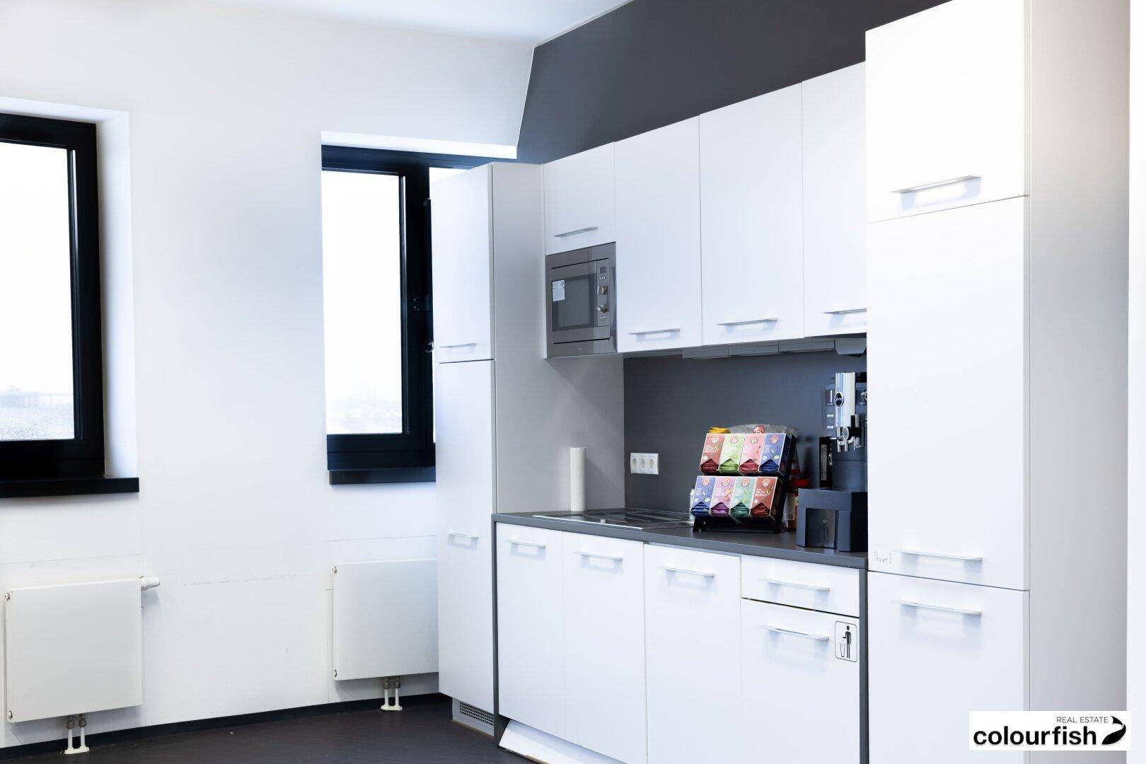 Moderne Teeküche mit weißen Schränken, Mikrowelle und Kaffeemaschine, ideal für Mitarbeiter.
