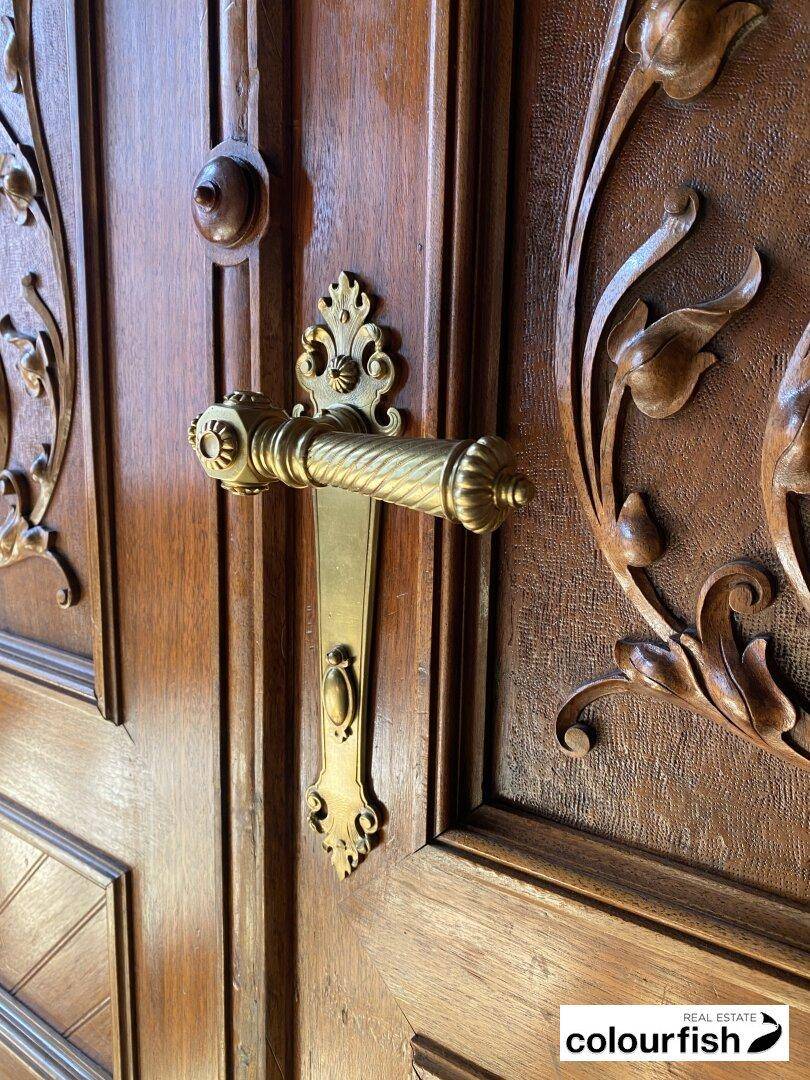 Detailansicht einer kunstvoll geschnitzten Holztür mit einem verzierten Messing-Türgriff im klassischen Stil.