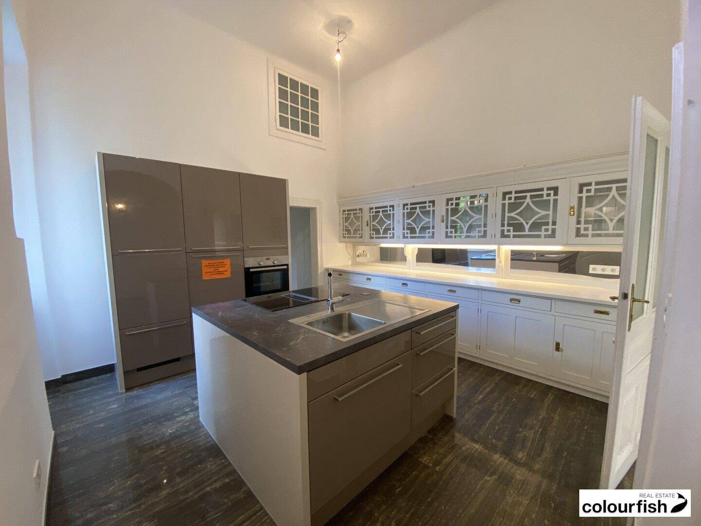 Moderne Küche mit grauer Kücheninsel, weißen Schränken, dunkler Arbeitsplatte und integriertem Backofen.