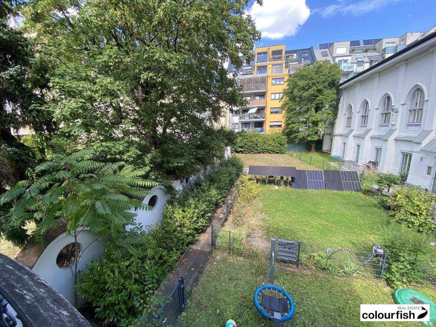 Großer Gartenbereich mit Rasenfläche, Bäumen, Sträuchern und Photovoltaik-Anlage im Hintergrund.