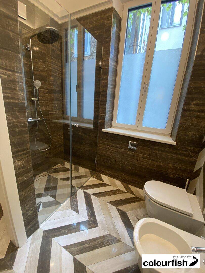 Elegantes Badezimmer mit begehbarer Dusche, WC, Bidet und auffälligem Fischgrätmuster auf dem Fliesenboden.