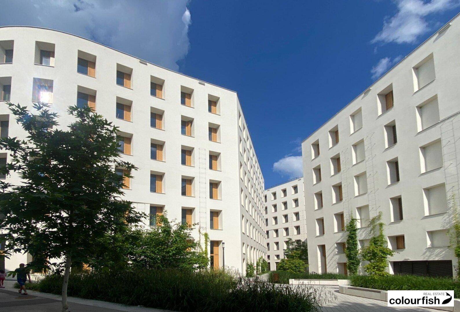 Mehrere moderne weiße Gebäude mit geschwungenen Fassaden, umgeben von Grünflächen und Bäumen.