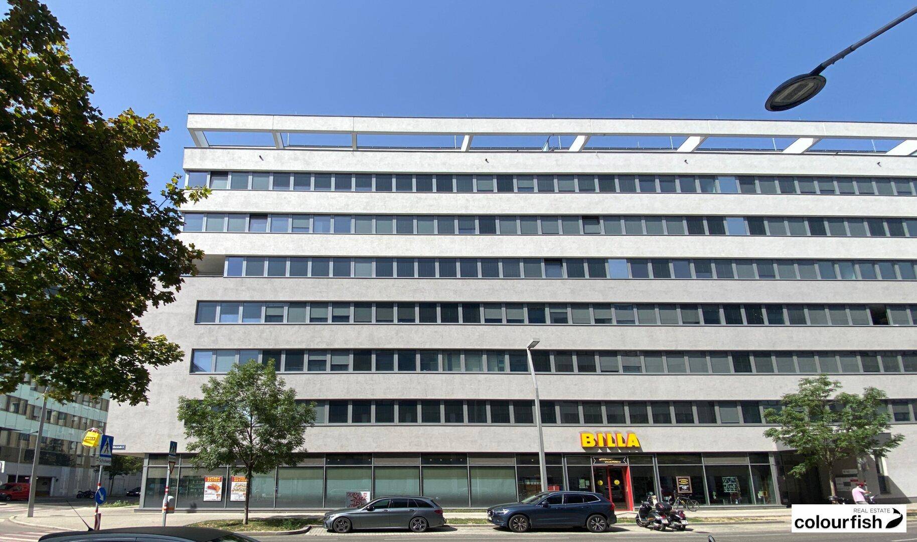 Modernes Geschäftsgebäude mit mehreren Etagen und Einzelhandelsflächen im Erdgeschoss, gut sichtbar von der Straße.