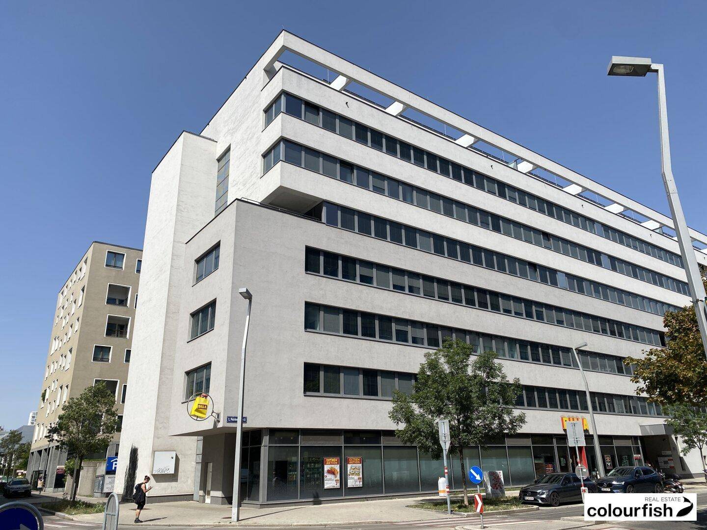 Zeitgenössisches Bürogebäude mit klaren Linien und großen Fensterfronten, umgeben von städtischer Infrastruktur.