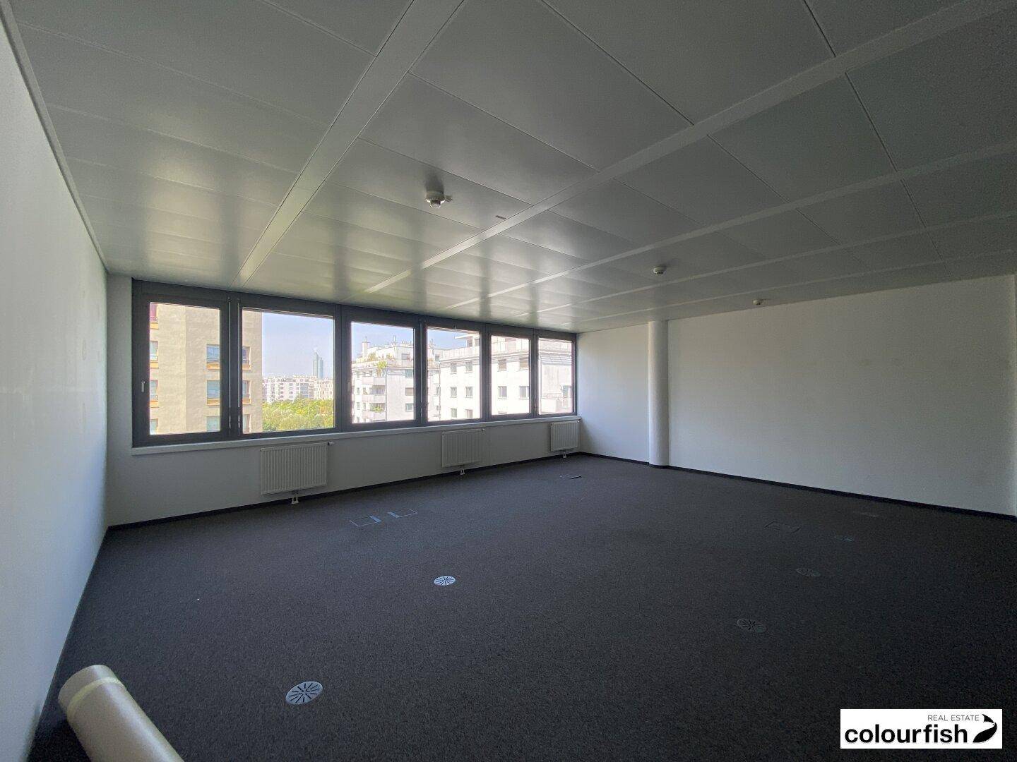 Großer, heller Büroraum mit Teppichboden und Blick auf die umliegenden Gebäude.