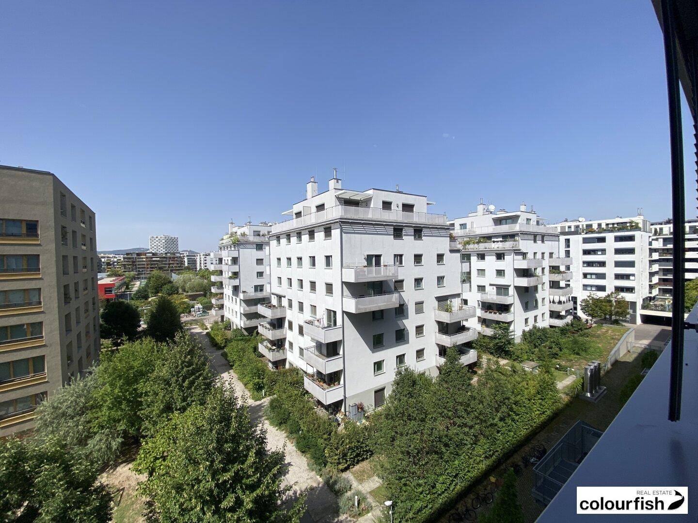Weitblick über eine Wohnsiedlung mit modernen Gebäuden und begrünten Innenhöfen unter blauem Himmel.