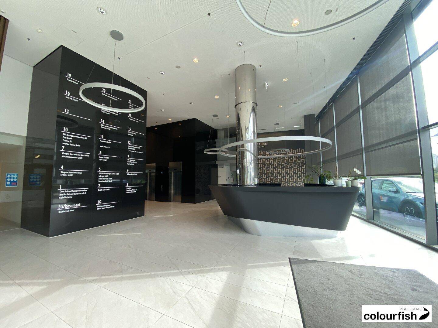Elegante Lobby mit modernem Empfangstresen, hohen Decken und großen Fenstern.