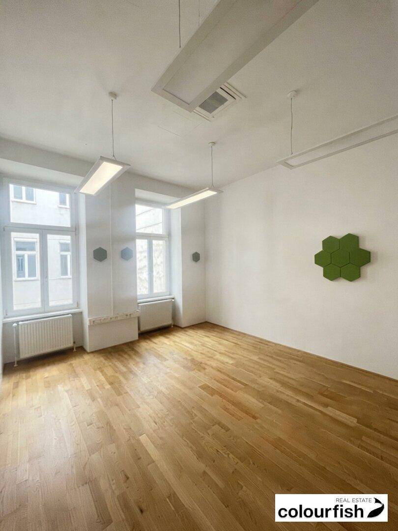 Geräumiger Büroraum mit Holzboden, großen Fenstern und schallabsorbierenden Wandpaneelen in Grün.