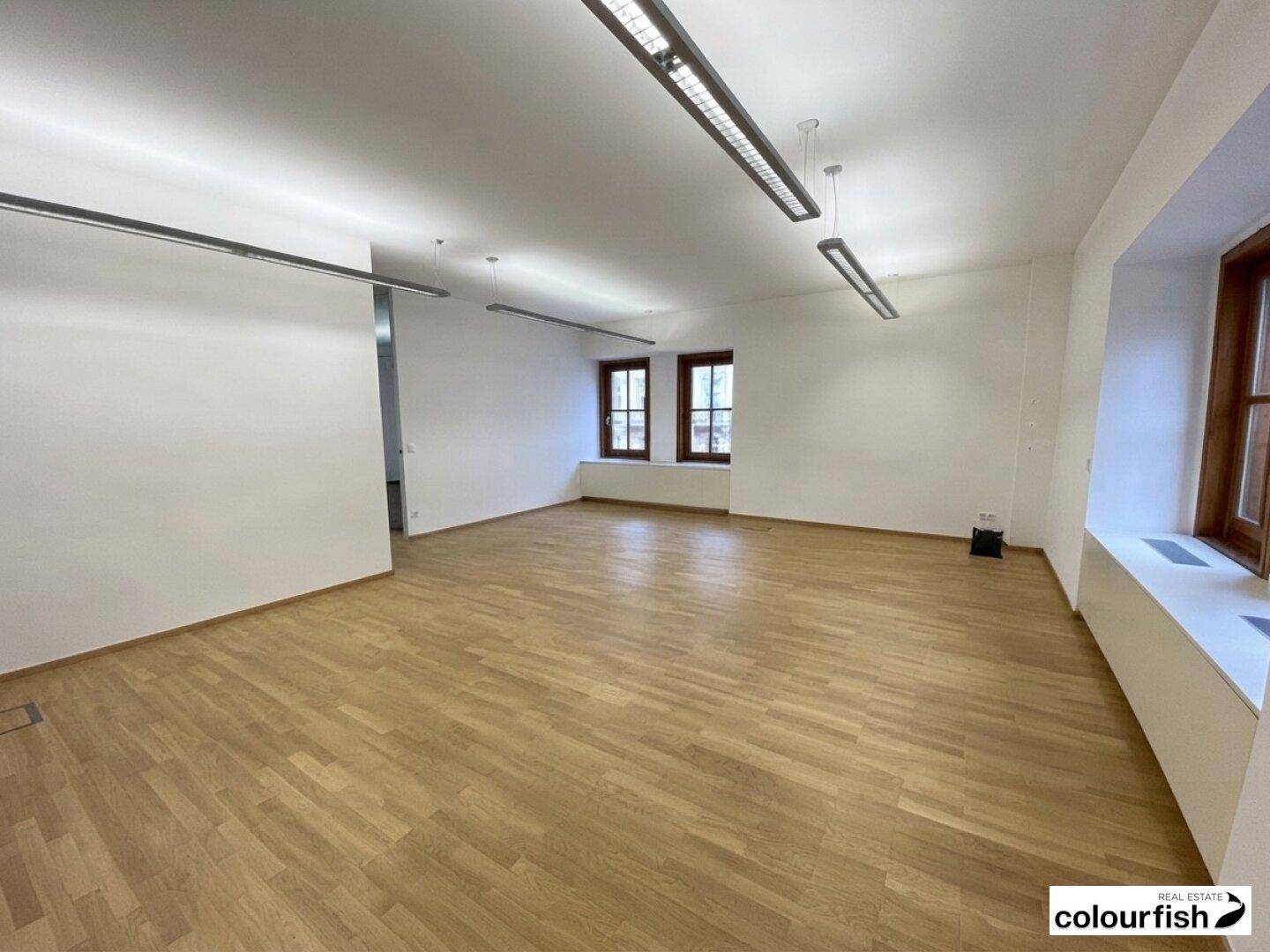 Großes, leeres Büro mit hellem Holzboden und mehreren Fenstern, bereit zur individuellen Gestaltung.