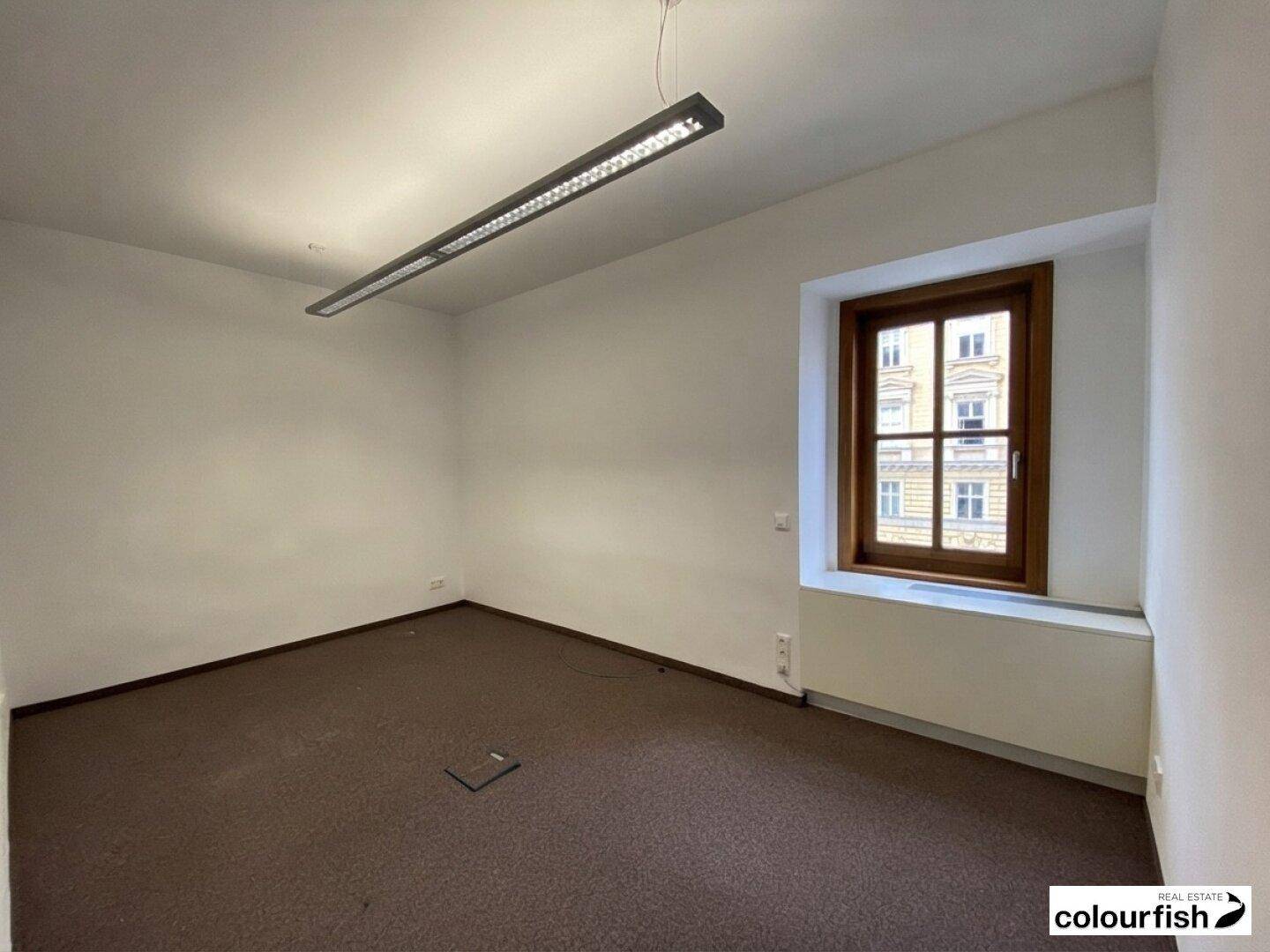 Kleineres Büro mit Teppichboden und einem Fenster, das für natürliches Licht sorgt.