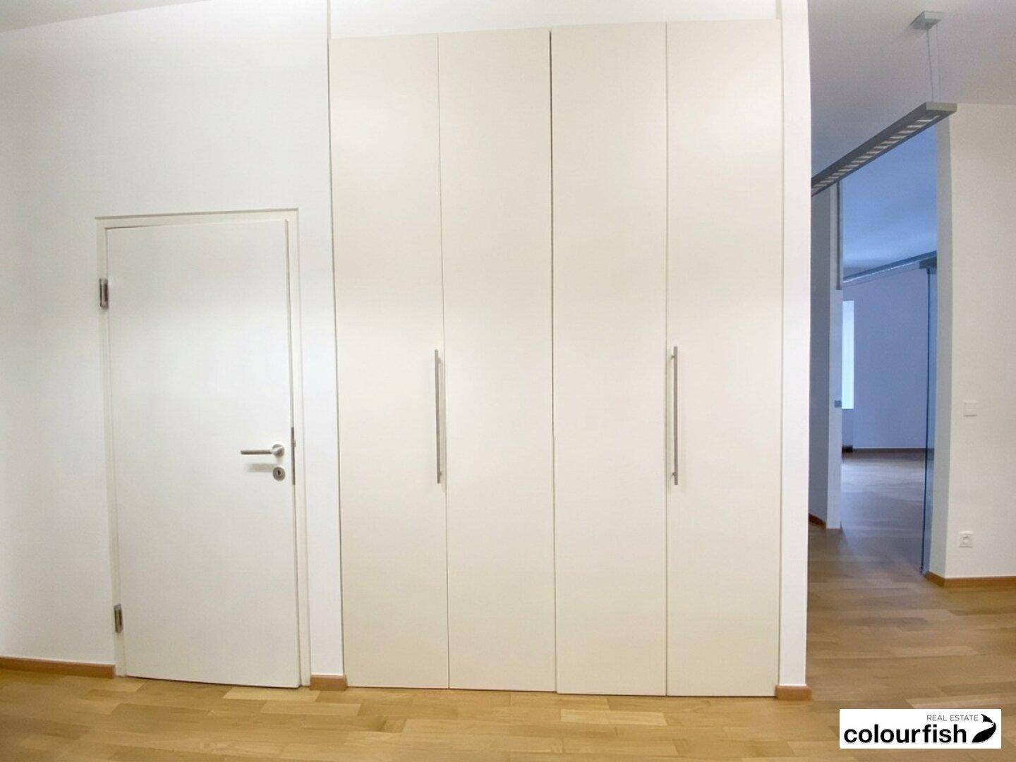 Heller Flur mit integrierten weißen Schränken und einer schlichten Tür, die den Raum funktional gestaltet.