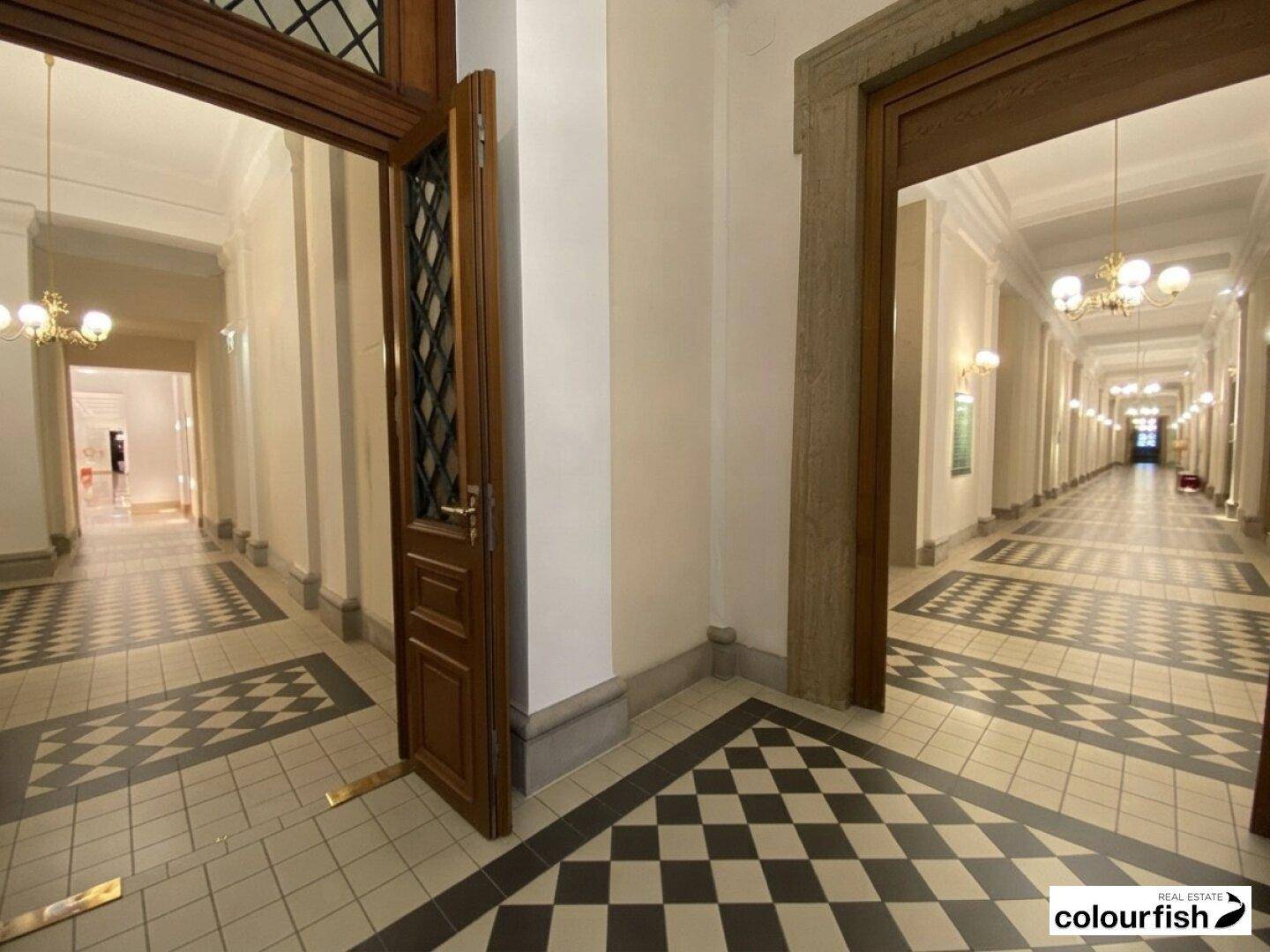 Eleganter Flur in einem historischen Gebäude mit Schachbrettmuster-Fliesen und opulenten Kronleuchtern.