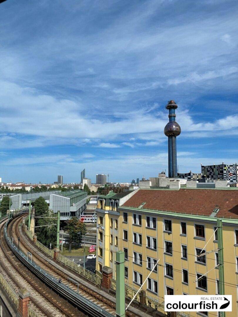 Panoramablick über die Stadt mit Bahngleisen, historischen Gebäuden und einem markanten Turm unter blauem Himmel.