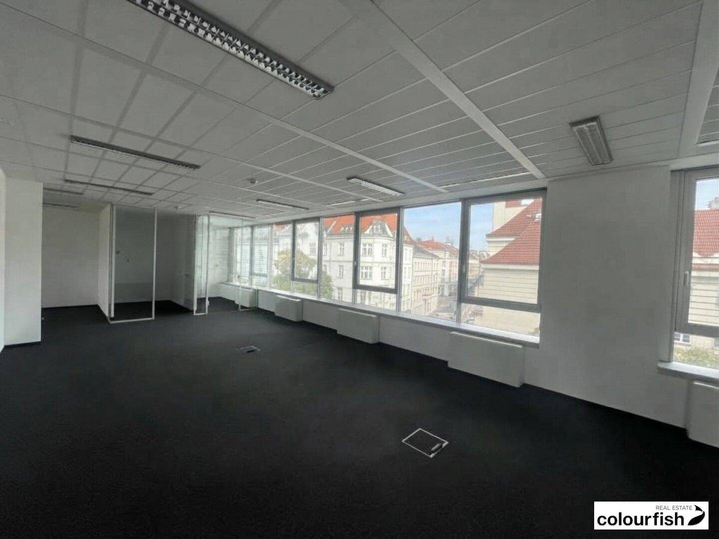 Heller Büroraum mit Teppichboden, großen Fenstern und Blick auf die umliegenden Stadtgebäude.